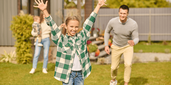 Niña jugando al aire libre con su familia en el jardín, una actividad divertida y económica para disfrutar juntos.