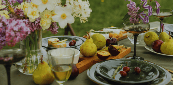 Vajilla y frutas dispuestas sobre una mesa en el jardín con decoración de flores alrededor. Ideal para celebrar una comida fresca y sabrosa en verano.