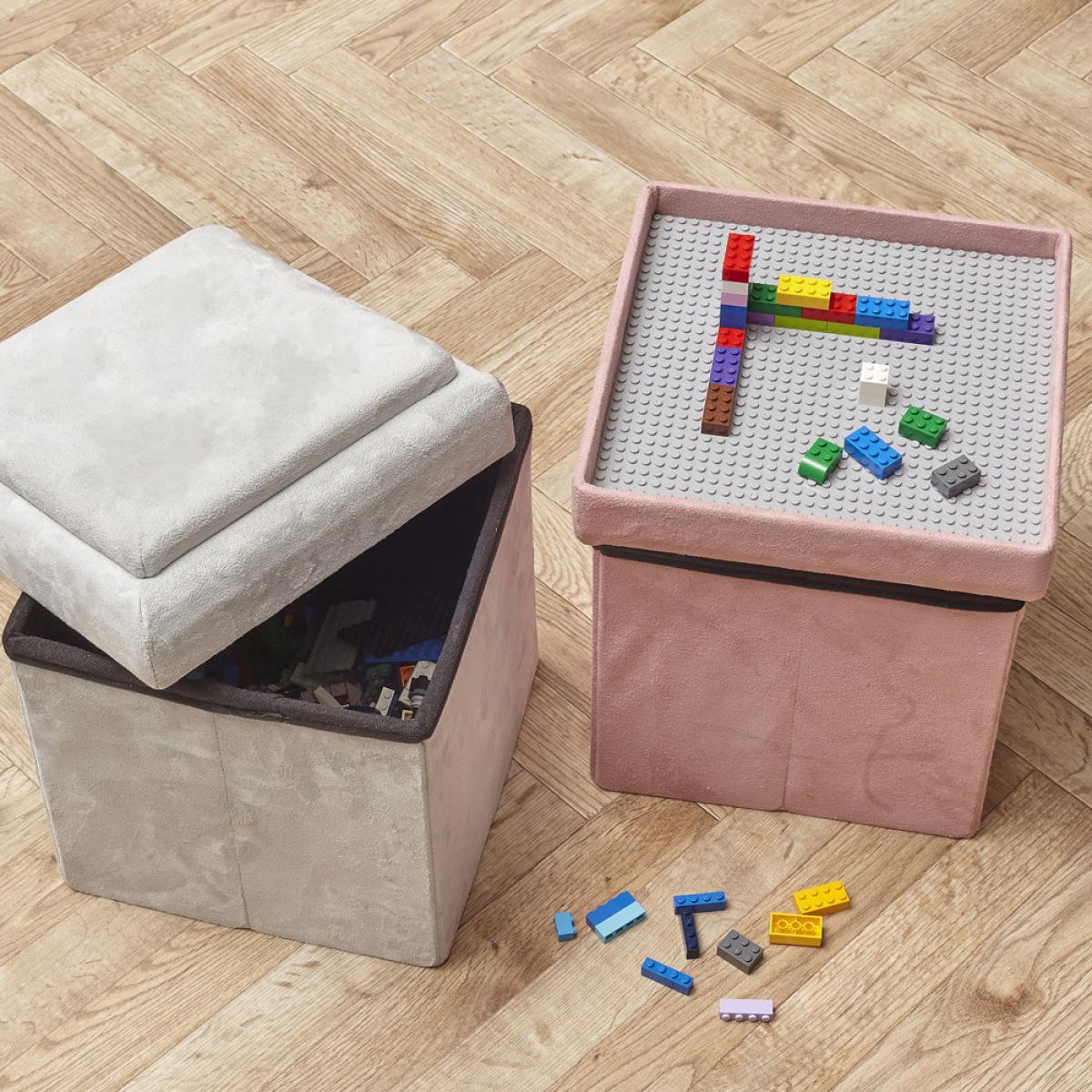 Caja puf plegable lego rosa con un panel compatible con las piezas de lego. abre la tapa, voltéala, encájala y ya está lista para usarla como base de las conatrucciones de lego. de madera mdf, textil acolchado y plástico. medidas: 27x27 cm; h.30 cm