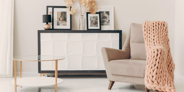 Espacio de salón con diseño emocional: sillón envolvente beige, manta tejida en tonos cálidos y mesa de centro con líneas suaves, rodeados de muebles de madera clara y decoración minimalista que transmiten calma, bienestar y armonía en el hogar.