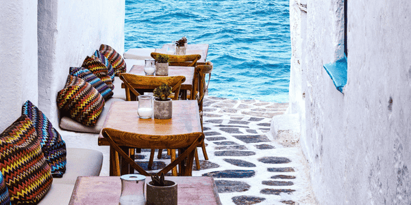 Camino en Mykonos con mesas y sofás y el mar en frente