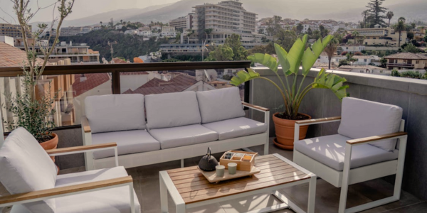 Terraza moderna con vistas a la ciudad, amueblada con un sofá y sillones blancos de exterior y una mesa de centro de madera.